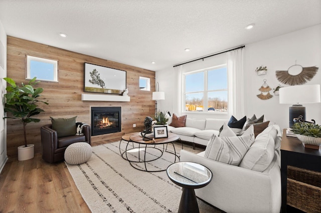 living area with recessed lighting, wood finished floors, wood walls, and a glass covered fireplace