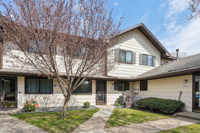 townhome / multi-family property featuring central air condition unit, a front lawn, and roof with shingles