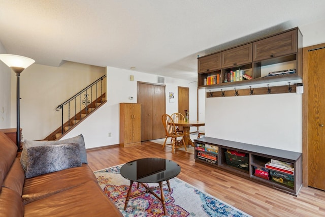 living room featuring visible vents, light wood-type flooring, and stairs