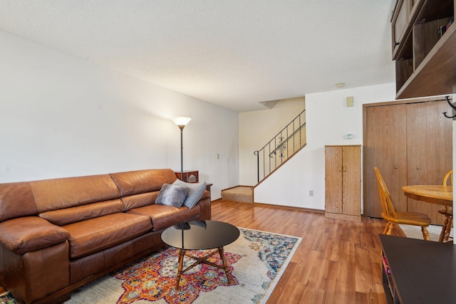 living area featuring baseboards, light wood finished floors, and stairway
