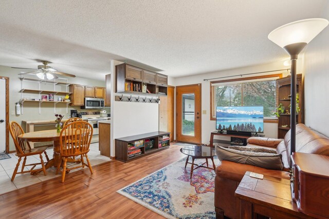 living room with a textured ceiling, light wood-style flooring, and ceiling fan