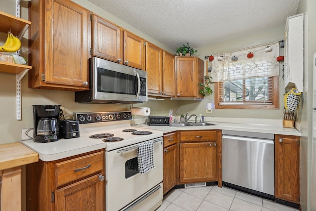 kitchen with brown cabinetry, open shelves, light countertops, a sink, and stainless steel appliances