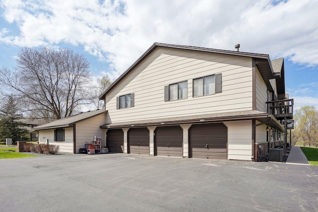 view of side of home featuring central air condition unit, an attached garage, driveway, and a balcony