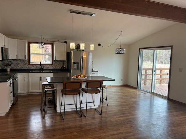 kitchen with dark countertops, tasteful backsplash, a sink, lofted ceiling, and appliances with stainless steel finishes
