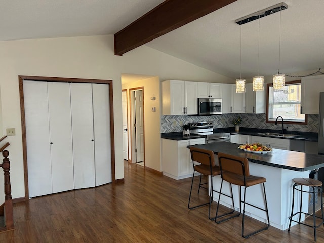 kitchen with dark countertops, a sink, lofted ceiling with beams, a kitchen bar, and appliances with stainless steel finishes