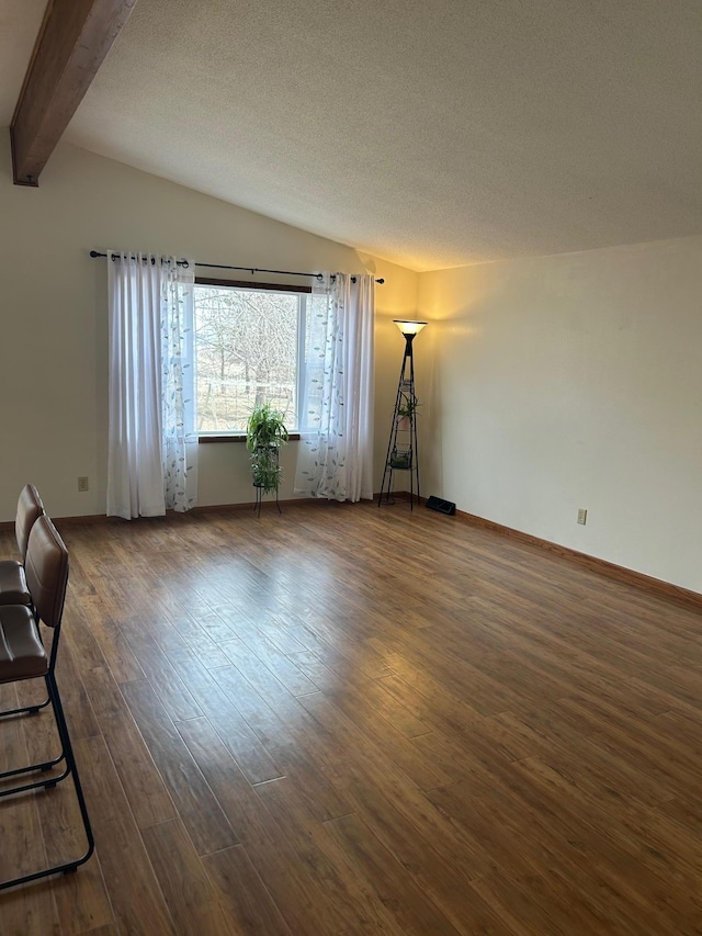 unfurnished living room featuring baseboards, dark wood-style flooring, vaulted ceiling with beams, and a textured ceiling