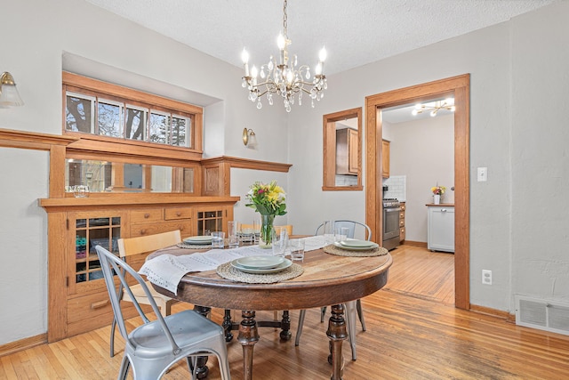 dining space with a chandelier, light wood finished floors, baseboards, and a textured ceiling