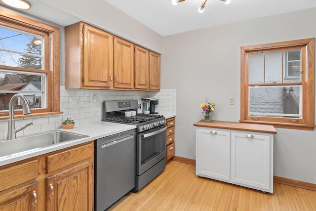 kitchen with appliances with stainless steel finishes, a sink, decorative backsplash, light wood-style floors, and light countertops