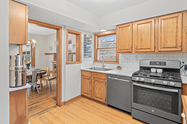 kitchen with stainless steel appliances, a sink, light wood-style flooring, a chandelier, and light countertops