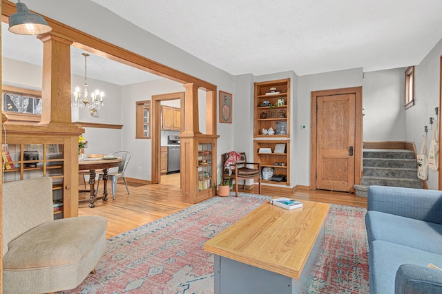 living area featuring light wood-type flooring, stairway, decorative columns, baseboards, and a chandelier