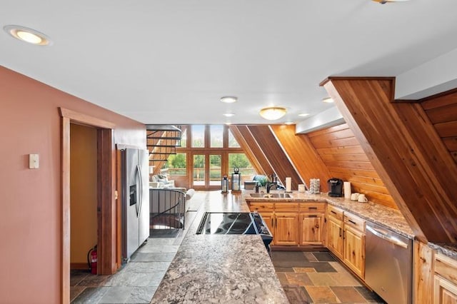 kitchen with a sink, stone tile flooring, appliances with stainless steel finishes, a peninsula, and light stone counters