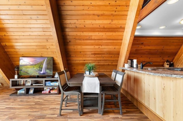 dining area with wooden walls, beamed ceiling, and wood finished floors