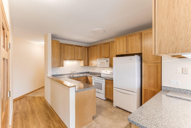 kitchen featuring a peninsula, a textured ceiling, white appliances, and a sink