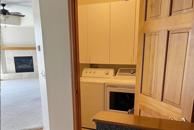 laundry room with ceiling fan, washer and clothes dryer, a tiled fireplace, carpet flooring, and cabinet space