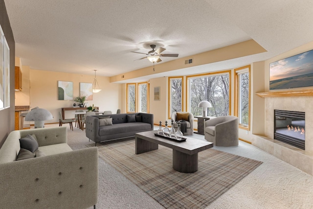 carpeted living room with a ceiling fan, a textured ceiling, visible vents, and a fireplace