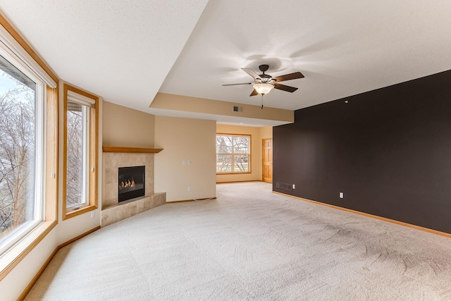 unfurnished living room with a tiled fireplace, a ceiling fan, baseboards, and carpet flooring