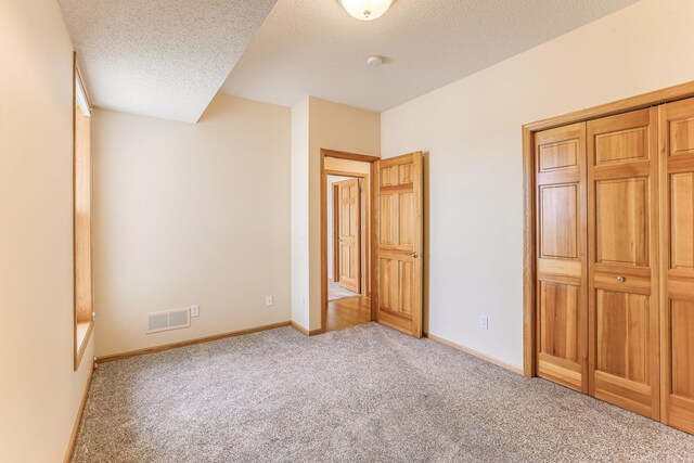 unfurnished bedroom with visible vents, a textured ceiling, carpet, and baseboards