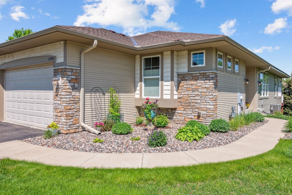 view of home's exterior featuring a garage, driveway, stone siding, and a shingled roof
