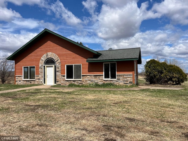 view of front facade featuring roof with shingles, a front yard, and stone siding