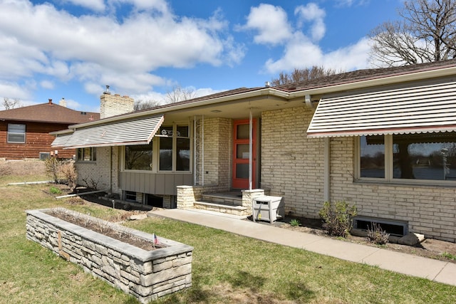back of property with a chimney, a lawn, and brick siding