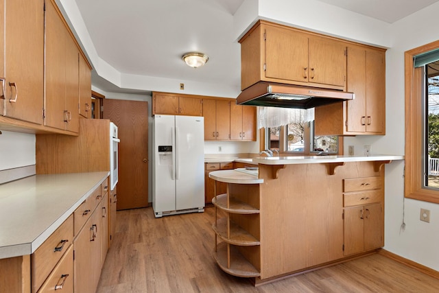 kitchen with white appliances, a peninsula, under cabinet range hood, light wood-type flooring, and light countertops