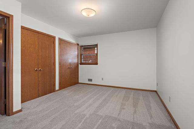 unfurnished bedroom featuring two closets, light colored carpet, and baseboards