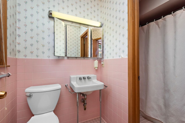 bathroom featuring wainscoting, toilet, wallpapered walls, and tile walls