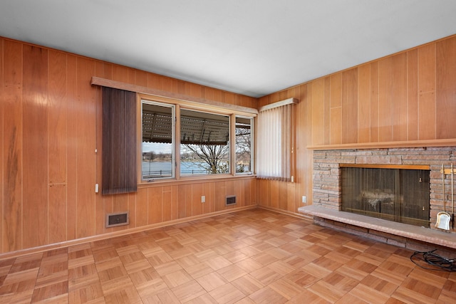 unfurnished living room featuring baseboards, wooden walls, and a stone fireplace