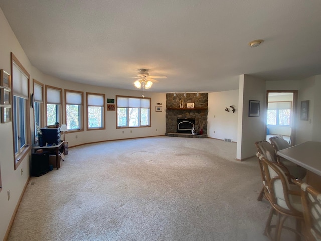 living room featuring a ceiling fan, baseboards, a fireplace, and light colored carpet