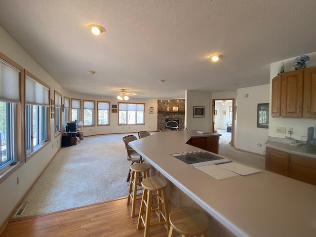 kitchen featuring a kitchen breakfast bar, a stone fireplace, visible vents, a ceiling fan, and open floor plan