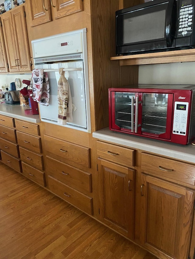 kitchen featuring light wood-type flooring, white oven, brown cabinetry, black microwave, and light countertops
