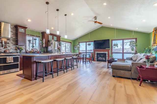 918 Division St, Elbow Lake, MN 56531 - kitchen with wall chimney range hood, appliances with stainless steel finishes, open floor plan, a breakfast bar, and light wood-style floors