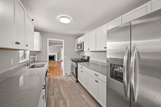 4240 Lake Road Ave, Robbinsdale, MN 55422 - kitchen with a sink, light wood-type flooring, white cabinetry, appliances with stainless steel finishes, and light stone countertops