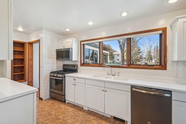 kitchen with stainless steel appliances, a sink, backsplash, white cabinetry, and light countertops