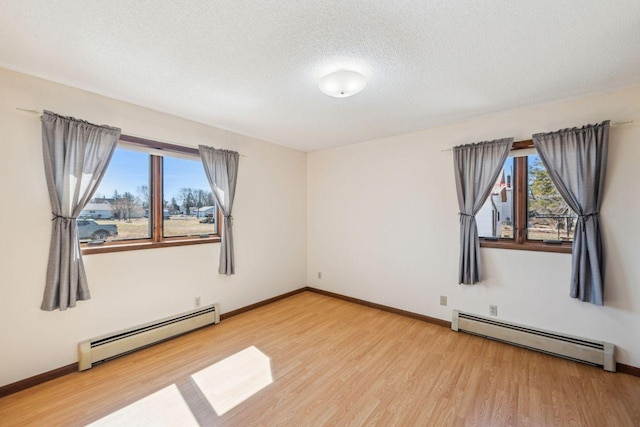 empty room featuring baseboard heating, a wealth of natural light, and light wood finished floors