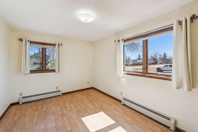 empty room with light wood-style floors, a textured ceiling, and baseboard heating