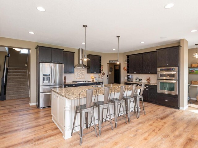 11460 Eagle Creek Ln, Rogers, MN 55374 - kitchen with stainless steel appliances, wall chimney range hood, backsplash, a kitchen bar, and light wood-type flooring