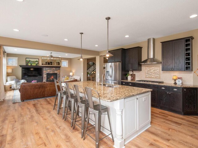 11460 Eagle Creek Ln, Rogers, MN 55374 - kitchen with wall chimney range hood, appliances with stainless steel finishes, a sink, light wood-style flooring, and a breakfast bar area