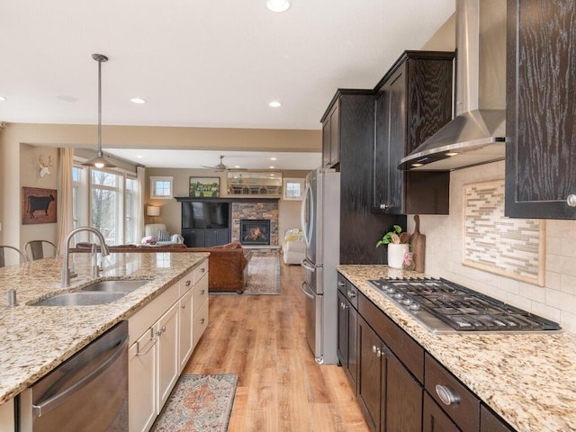 11460 Eagle Creek Ln, Rogers, MN 55374 - kitchen featuring stainless steel appliances, wall chimney range hood, a sink, ceiling fan, and a fireplace