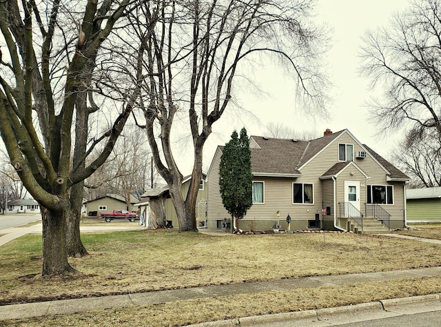 view of front facade featuring roof with shingles, a front yard, a chimney, and entry steps