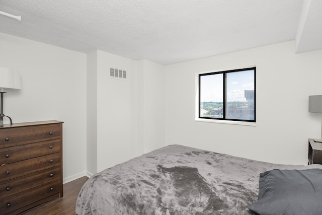bedroom featuring baseboards, visible vents, a textured ceiling, and dark wood finished floors