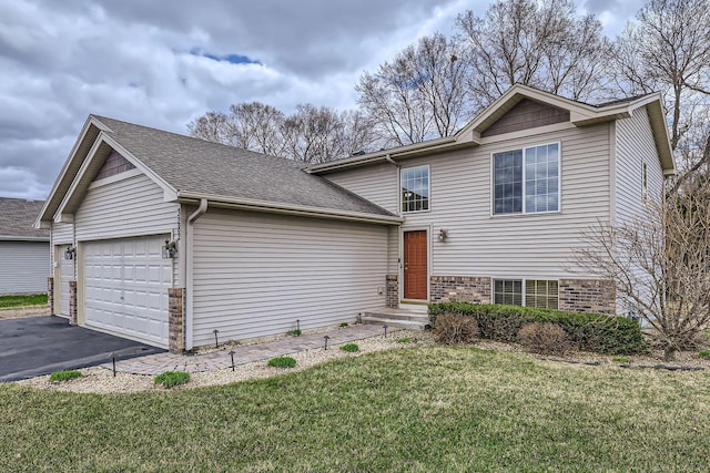 split level home featuring a front yard, a garage, a shingled roof, aphalt driveway, and brick siding