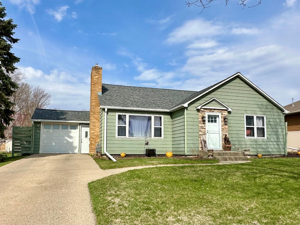 ranch-style home with driveway, a chimney, a front yard, a garage, and a shingled roof