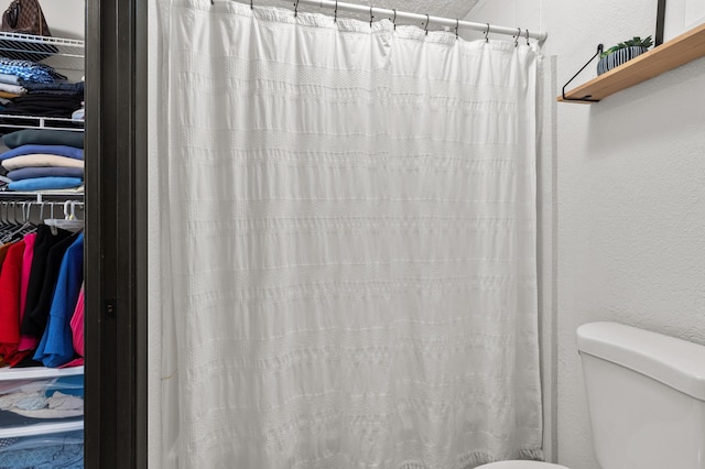 full bath featuring toilet, a textured wall, and a shower with shower curtain