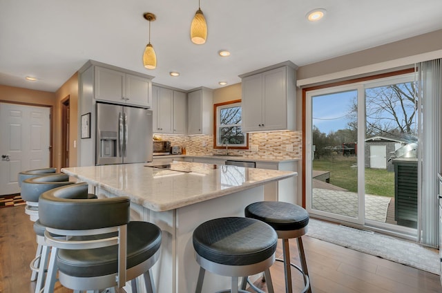 kitchen featuring backsplash, appliances with stainless steel finishes, wood finished floors, gray cabinetry, and a sink