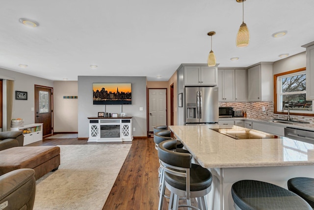 kitchen featuring light stone counters, a sink, gray cabinets, stainless steel appliances, and open floor plan