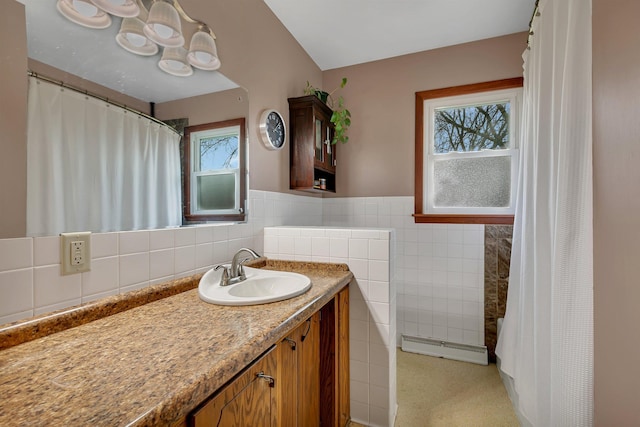 full bathroom featuring vanity, a wainscoted wall, baseboard heating, and tile walls
