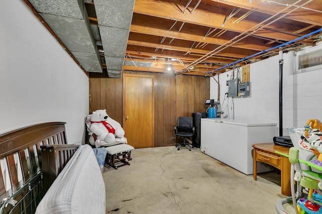 unfinished below grade area featuring wooden walls, refrigerator, and electric panel