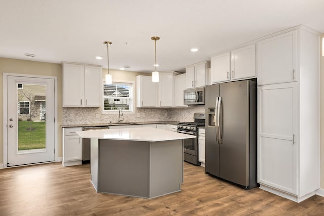 kitchen with appliances with stainless steel finishes, a sink, a center island, white cabinetry, and decorative backsplash
