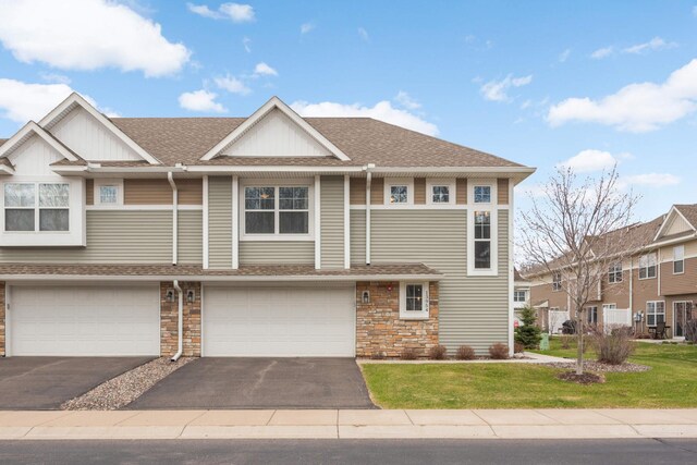 multi unit property featuring an attached garage, driveway, a shingled roof, and a front lawn